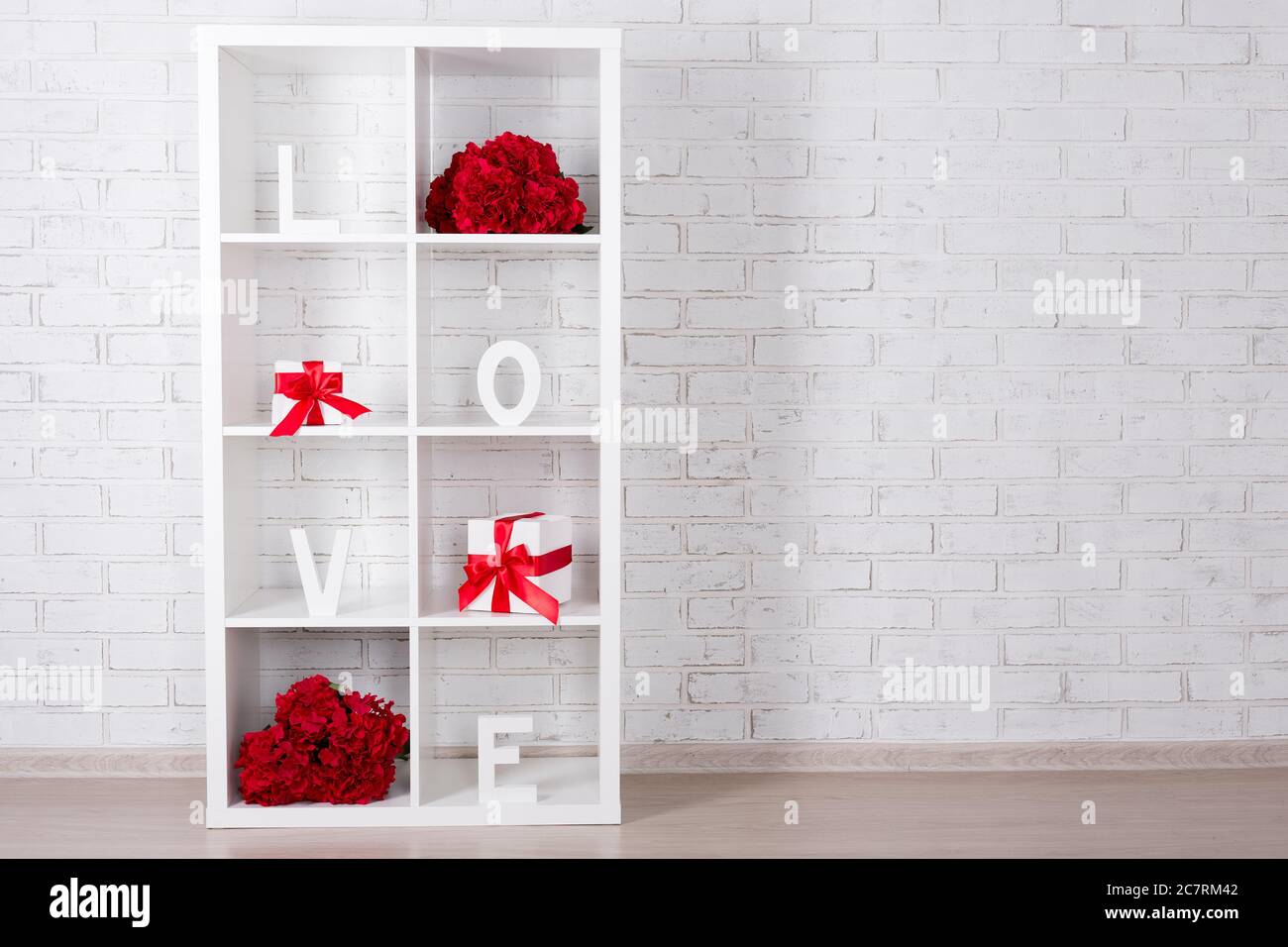 modern wooden shelf with flowers and gifts over white brick wall ...