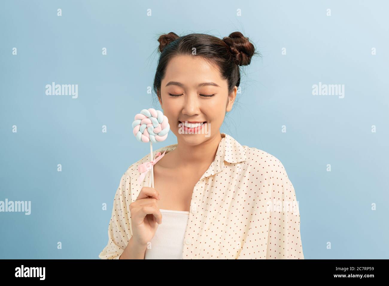 Fun lifestyle. Playful lady smiling holding lollipop isolated on blue background. Stock Photo