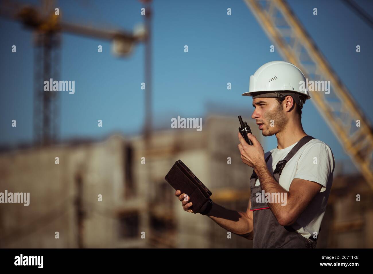 Engineer builder using tablet and walkie talkie, giving instructions at a construction site Stock Photo