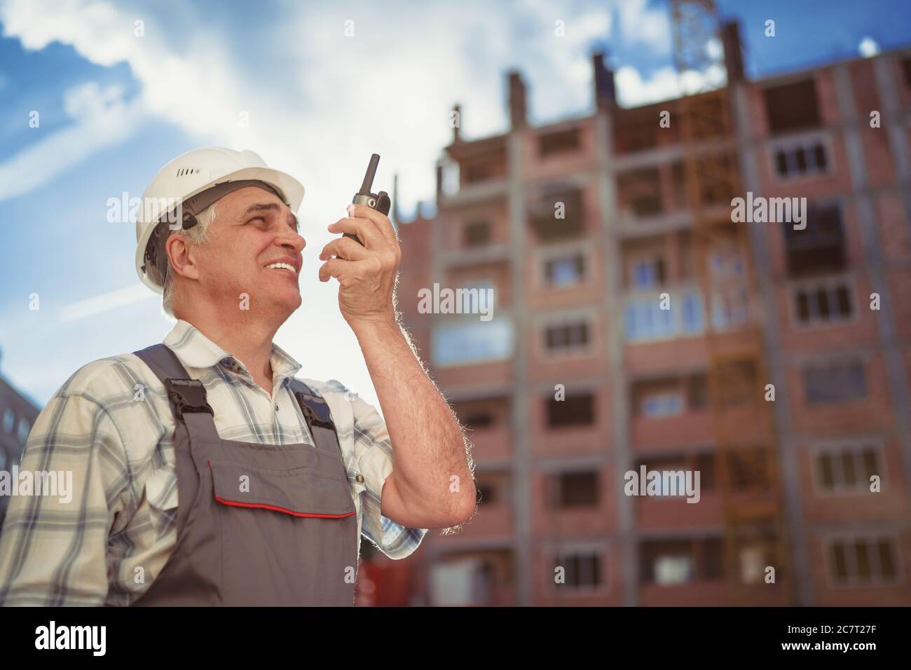 Senior engineer builder using a walkie talkie at a construction site. Sunset time Stock Photo