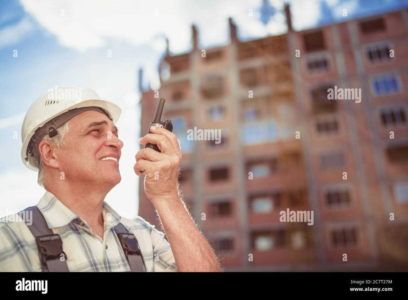 Senior engineer builder using a walkie talkie at a construction site. Sunset time Stock Photo