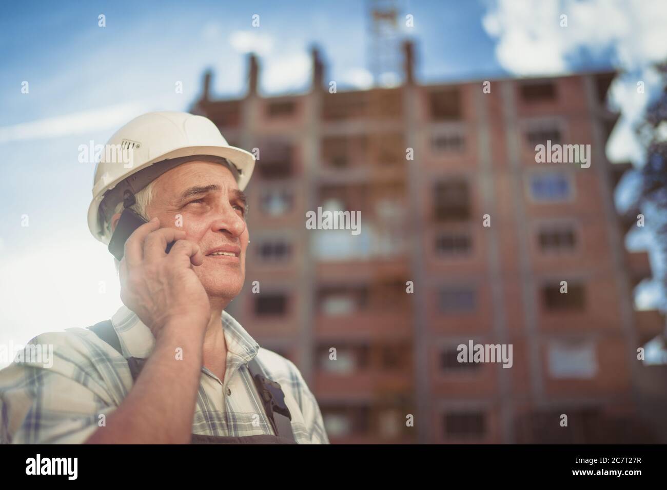 Senior engineer builder using a walkie talkie at a construction site. Sunset time Stock Photo