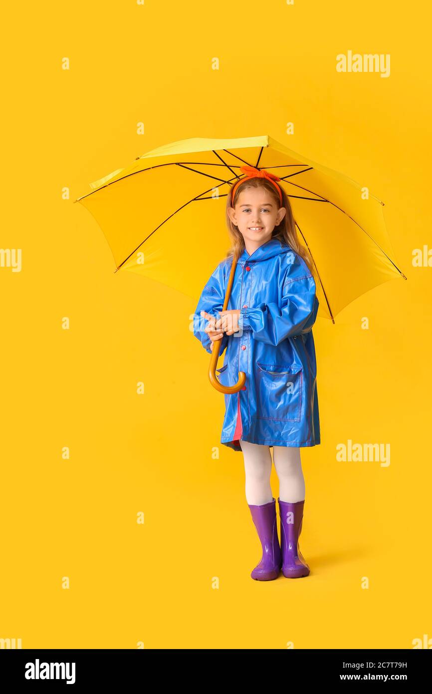 Cute little girl in raincoat and with umbrella on color background