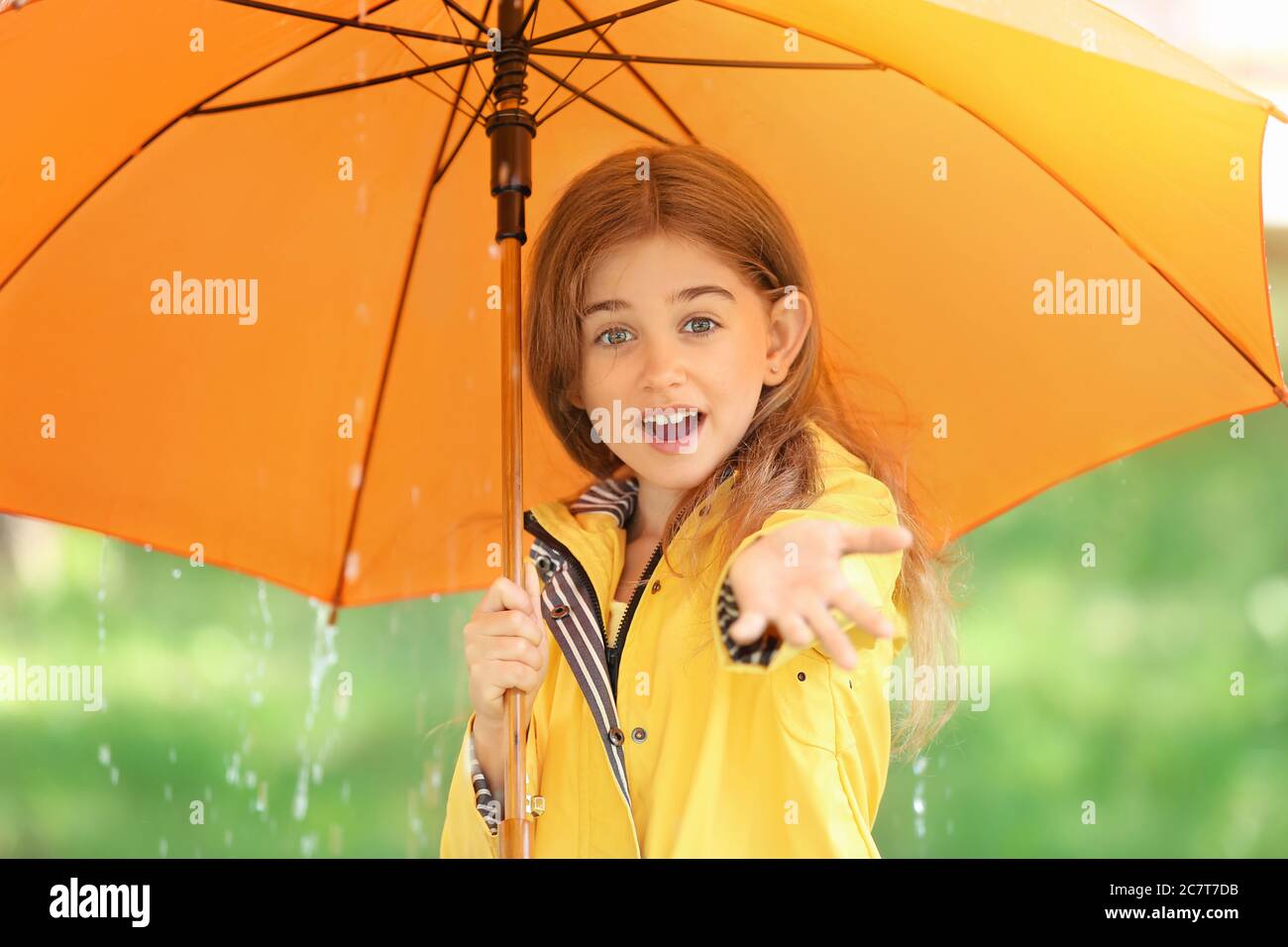 Cute little girl with umbrella wearing raincoat in park Stock