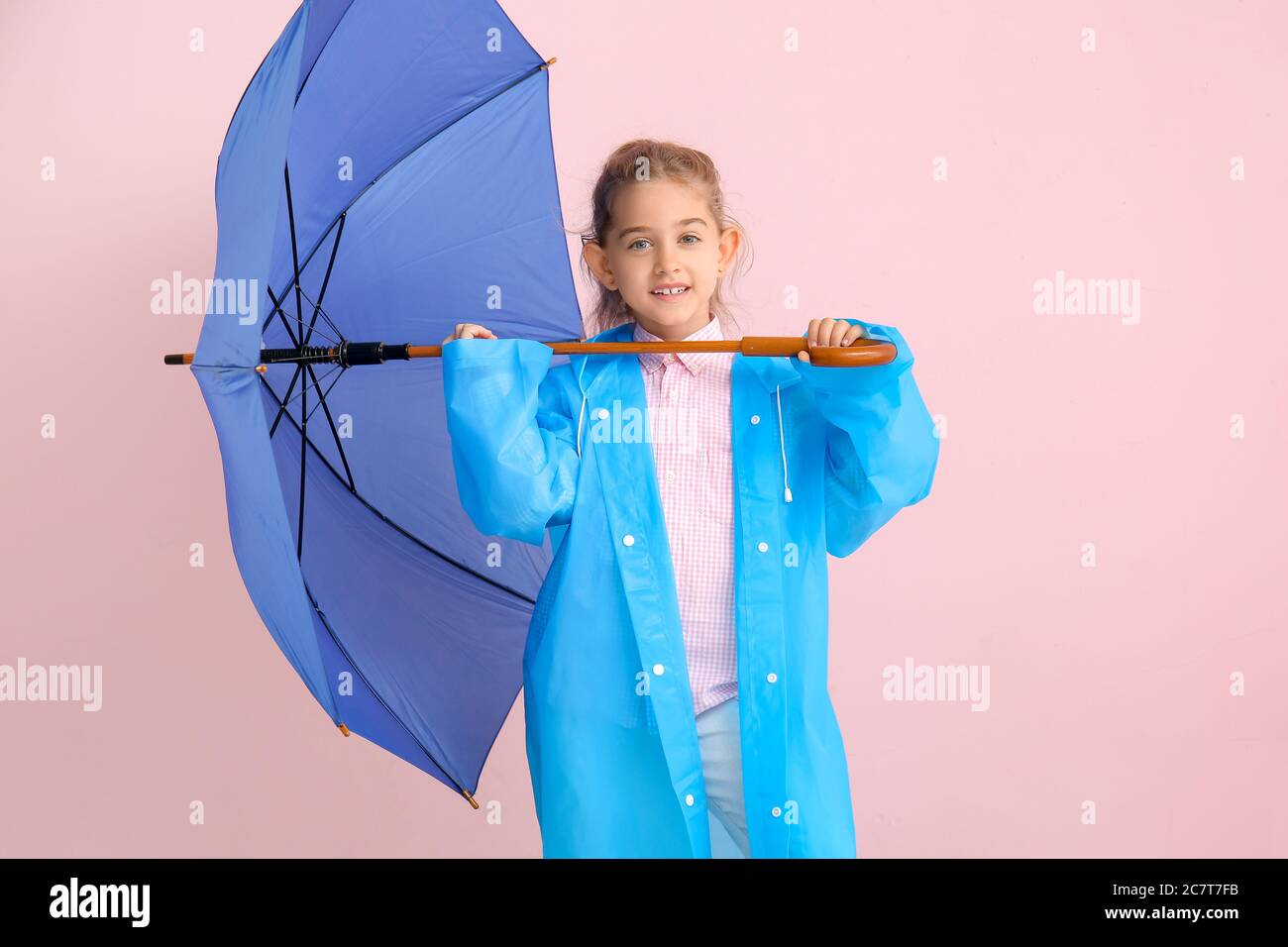 Cute little girl in raincoat and with umbrella on color background