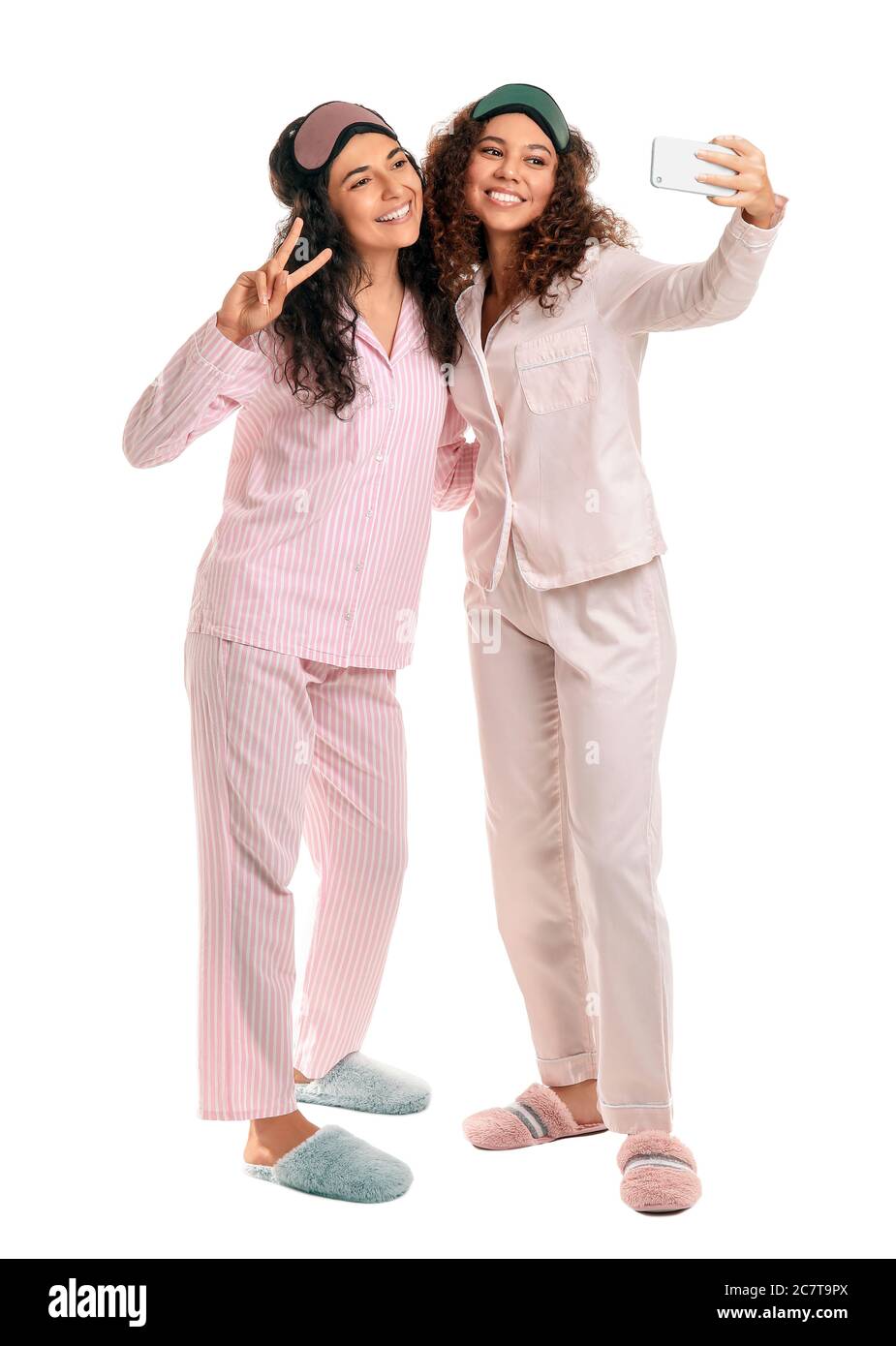 Beautiful young women in pajamas taking selfie on white background ...