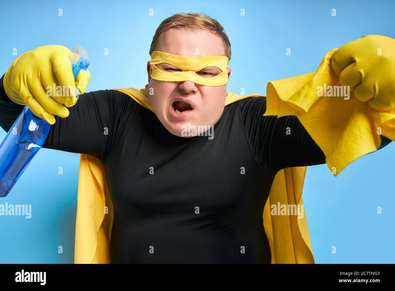 angry caucasian fat man in yellow costume applies detergent at camera and holds yellow rag in hands, he is tired of dirt. cleaning concept. isolated b Stock Photo
