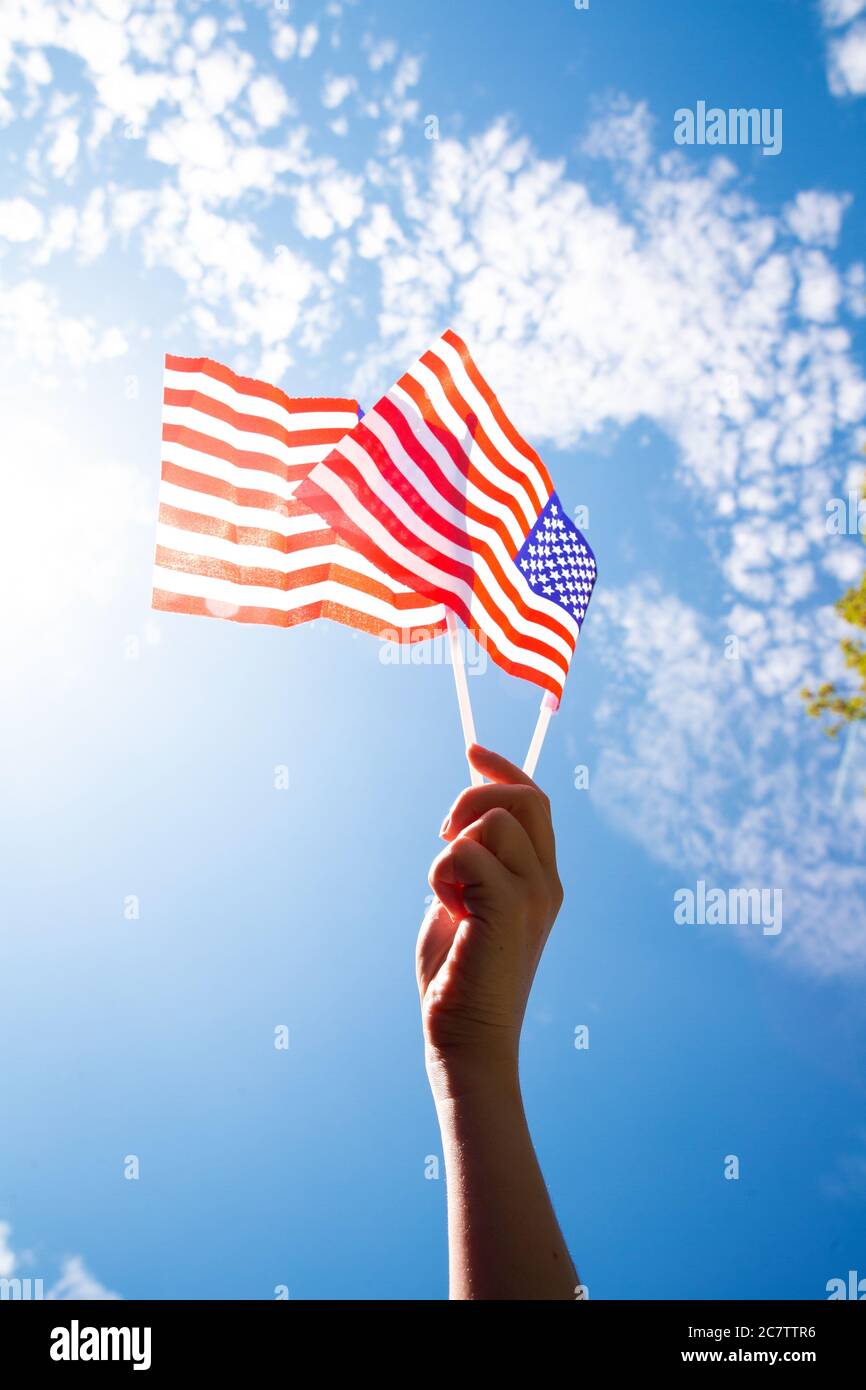 Hand holding two american flags on the blue sky with sunlight background, waving flag for United States of America close-up Stock Photo