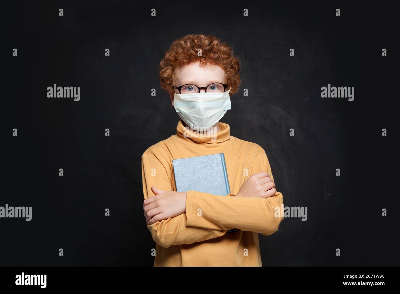 Clever child in medical protective face mask holding book on blackboard ...