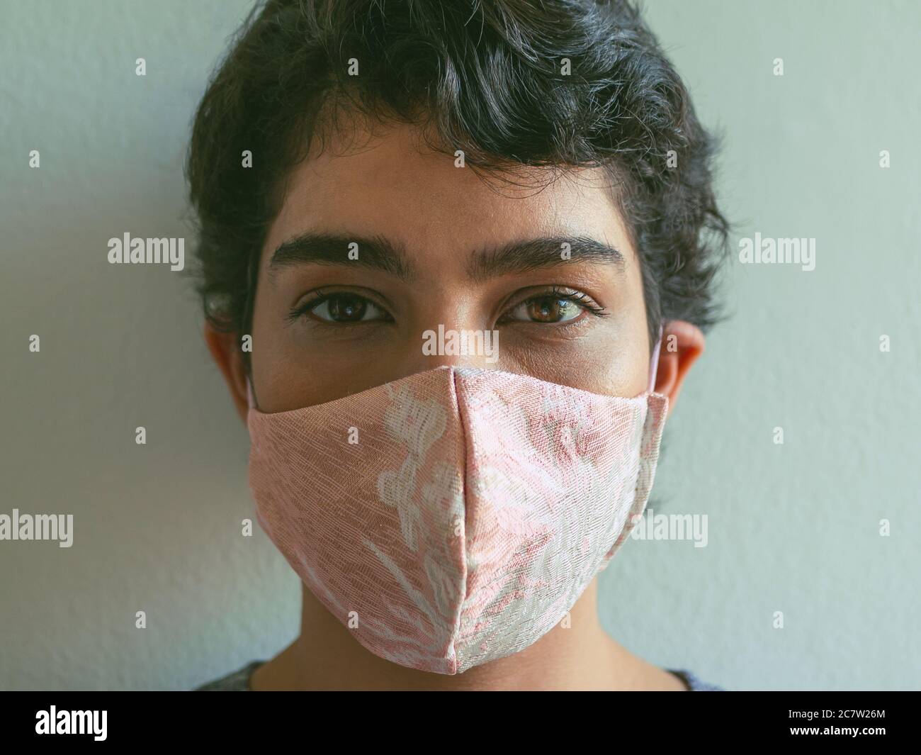 Short-haired woman wearing a pink face mask and looking at the camera. Stock Photo