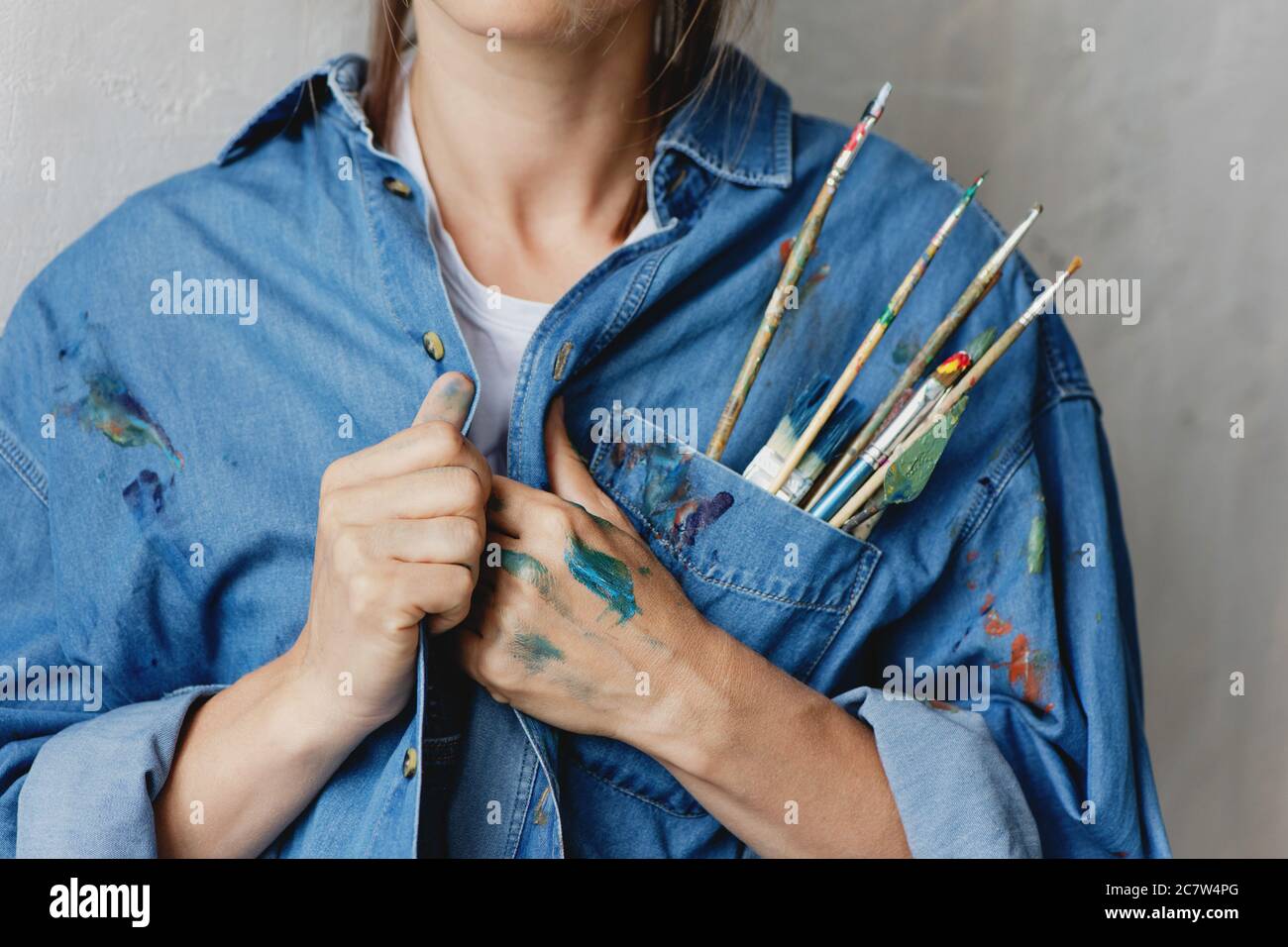 Cropped image of woman with paint brushes and palette knife placed in the pocket of her denim shirt. Stock Photo