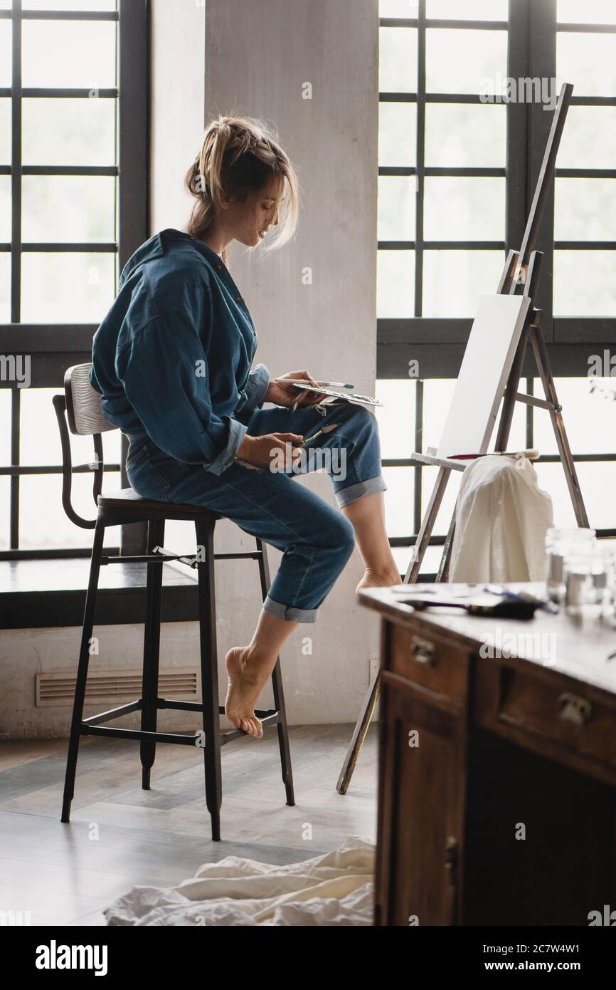 Beautiful blonde female artist painting picture in studio. Stock Photo