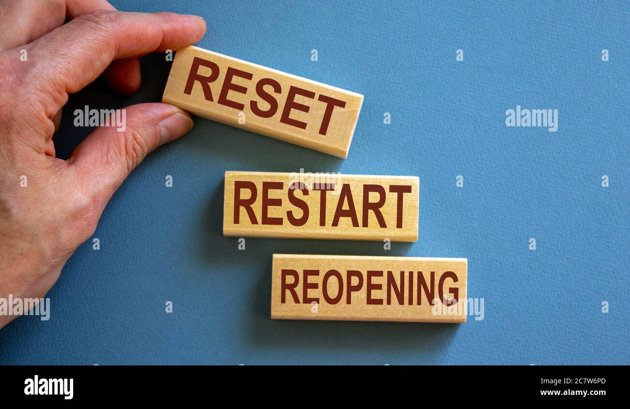 Wooden blocks form the words 'reset, restart, reopening' on blue background. Male hand. Stock Photo