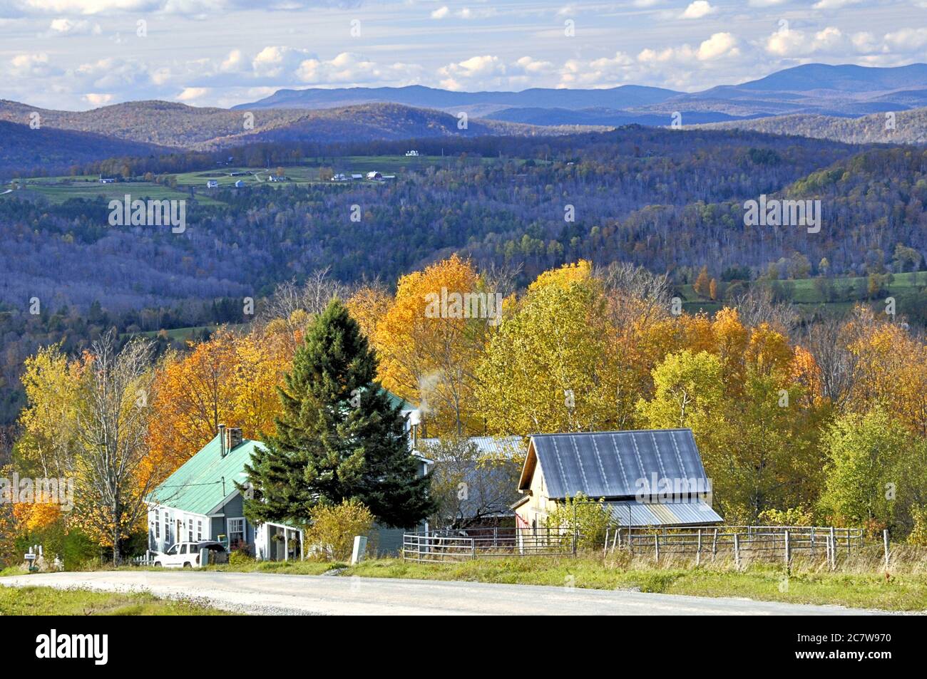 Quiet country road in Northeast Kingdom of rural Vermont with sweeping view of distant mountains, farm, hillside, and colorful autumn foliage. Stock Photo