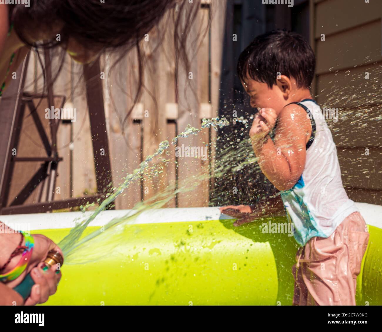Girl spraying boy with water hose. A backyard pool party at home with kids Stock Photo