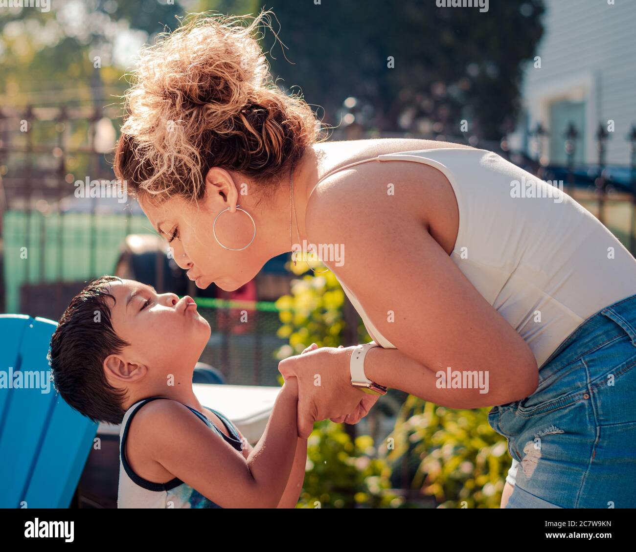 A mother is leaning to kiss her son on the lips at a backyard pool party Stock Photo