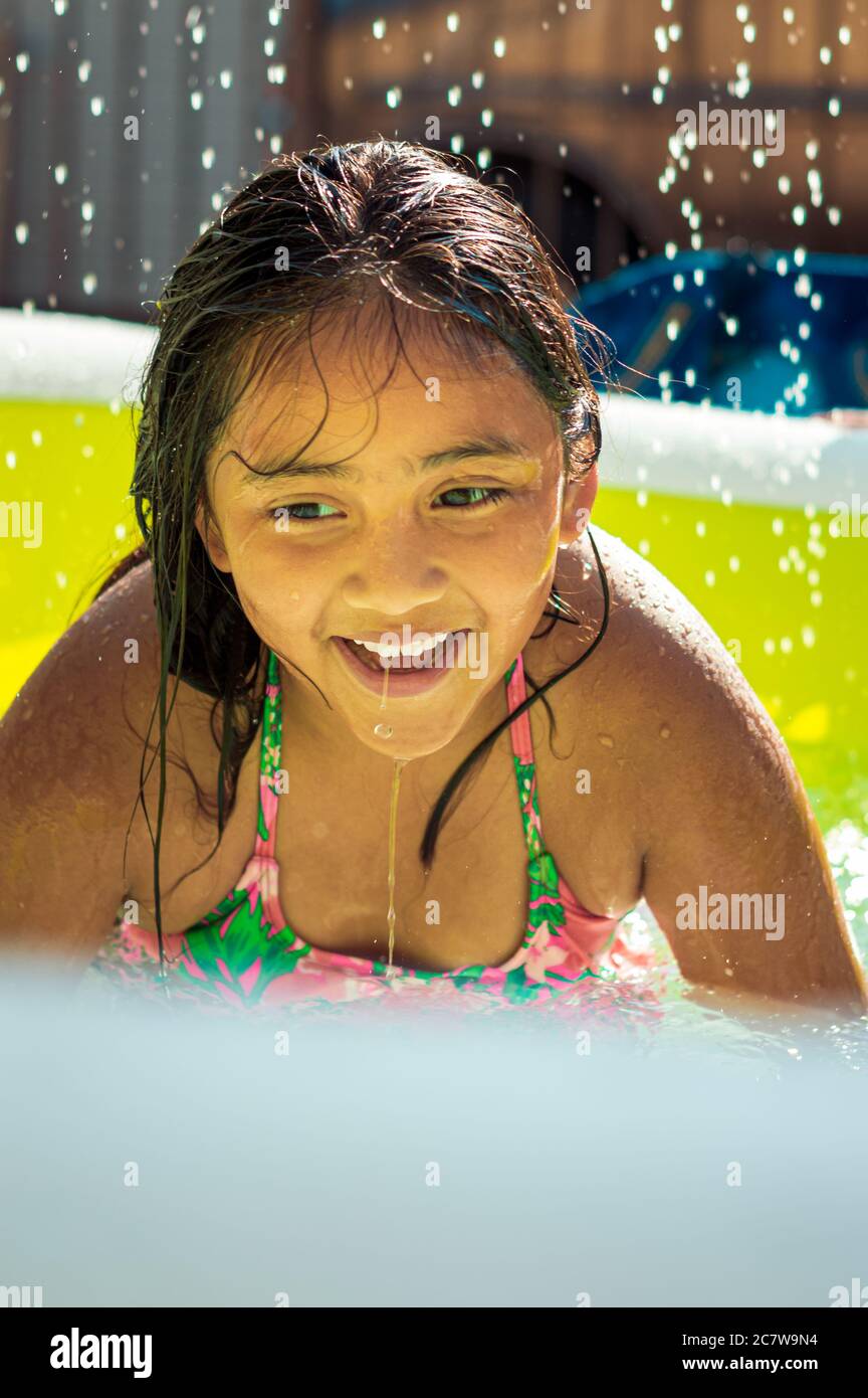 Girl is smiling and playing in swimming pool. A backyard pool party at home with kids Stock Photo