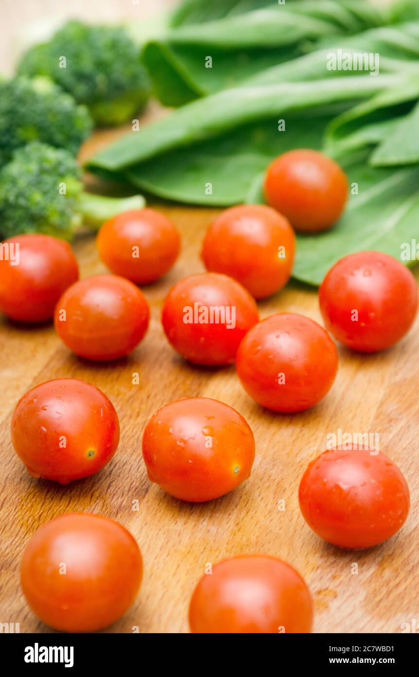Fresh organic Tomato, with background vegetables in wooden chop board. Stock Photo