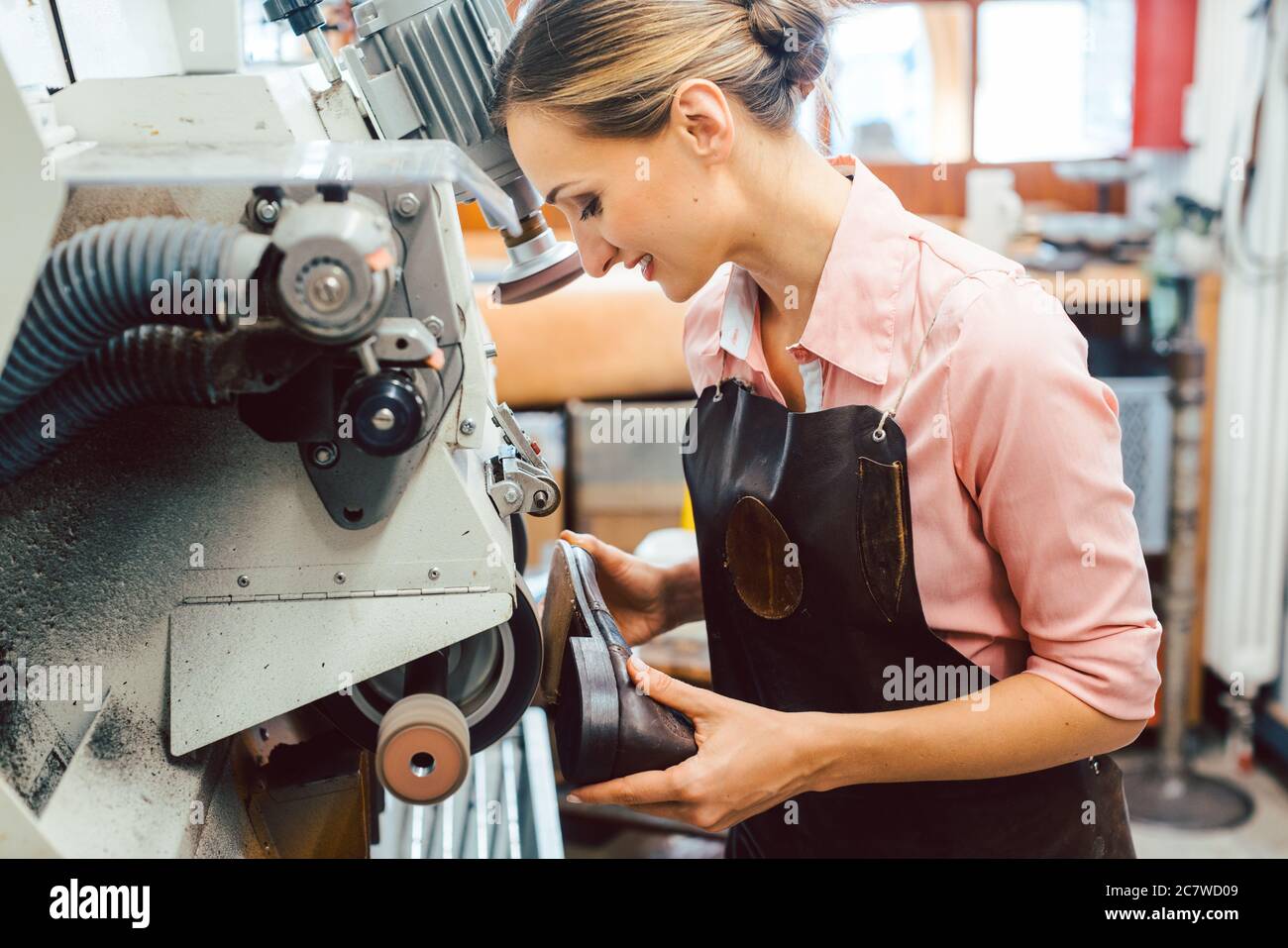 Woman cobbler working on machine in her shoemaker workshop Stock Photo