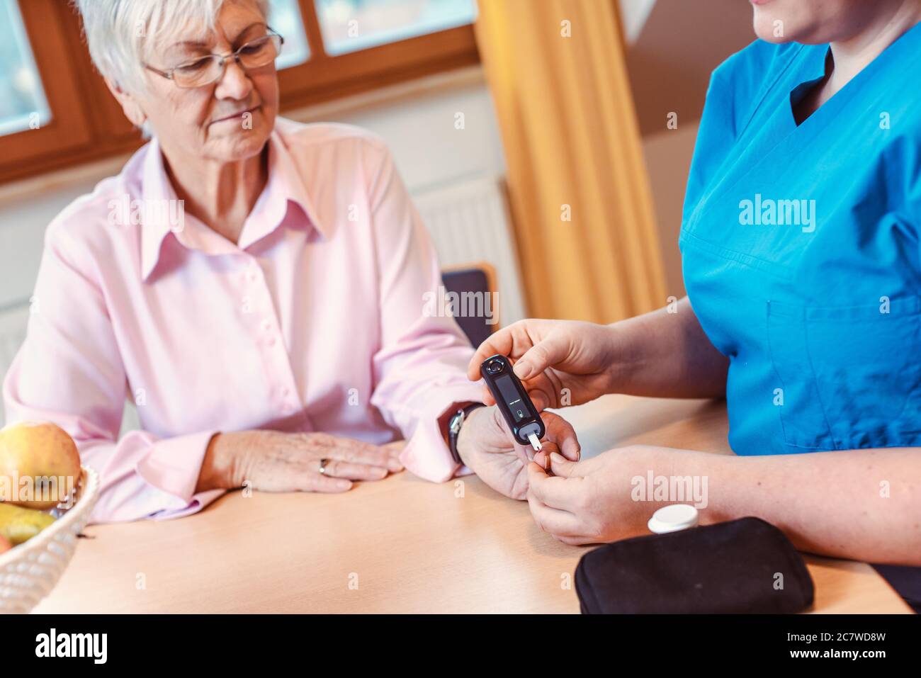 Nurse administers diabetes test to senior in nursing home Stock Photo