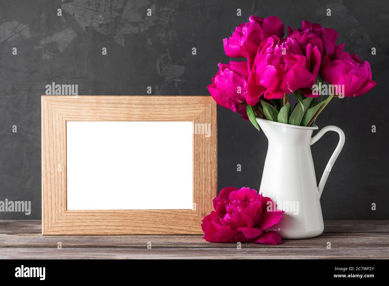 Blank photo frame with red peony flowers bouquet on rustic wooden table. still life. mock up. wedding or holiday concept. festive background Stock Photo