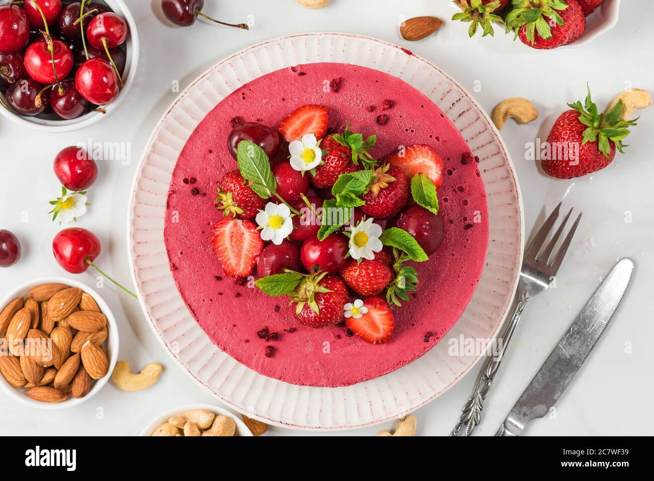 Berry cheesecake with fresh strawberries, cherries and flowers on white background with knife and fork. top view. healthy vegan food dessert Stock Photo