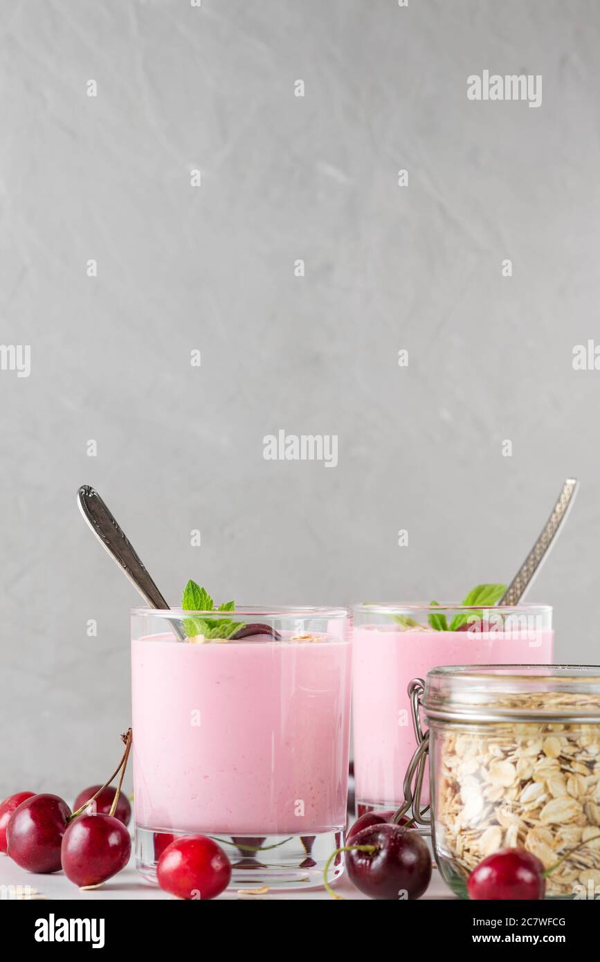 Cherry yogurt with fresh berries, oats and mint in glasses with spoons on white background. Healthy diet breakfast. vertical orientation. close up Stock Photo