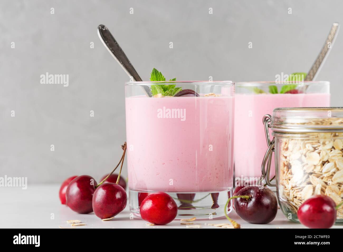 Cherry yogurt with fresh berries, oats and mint in glasses with spoons on white background. Healthy diet breakfast. close up Stock Photo