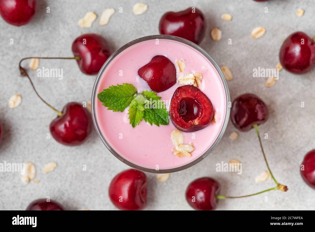 Glass of healthy cherry yogurt with fresh berries, oats and mint on white marble table. healthy breakfast. top view Stock Photo