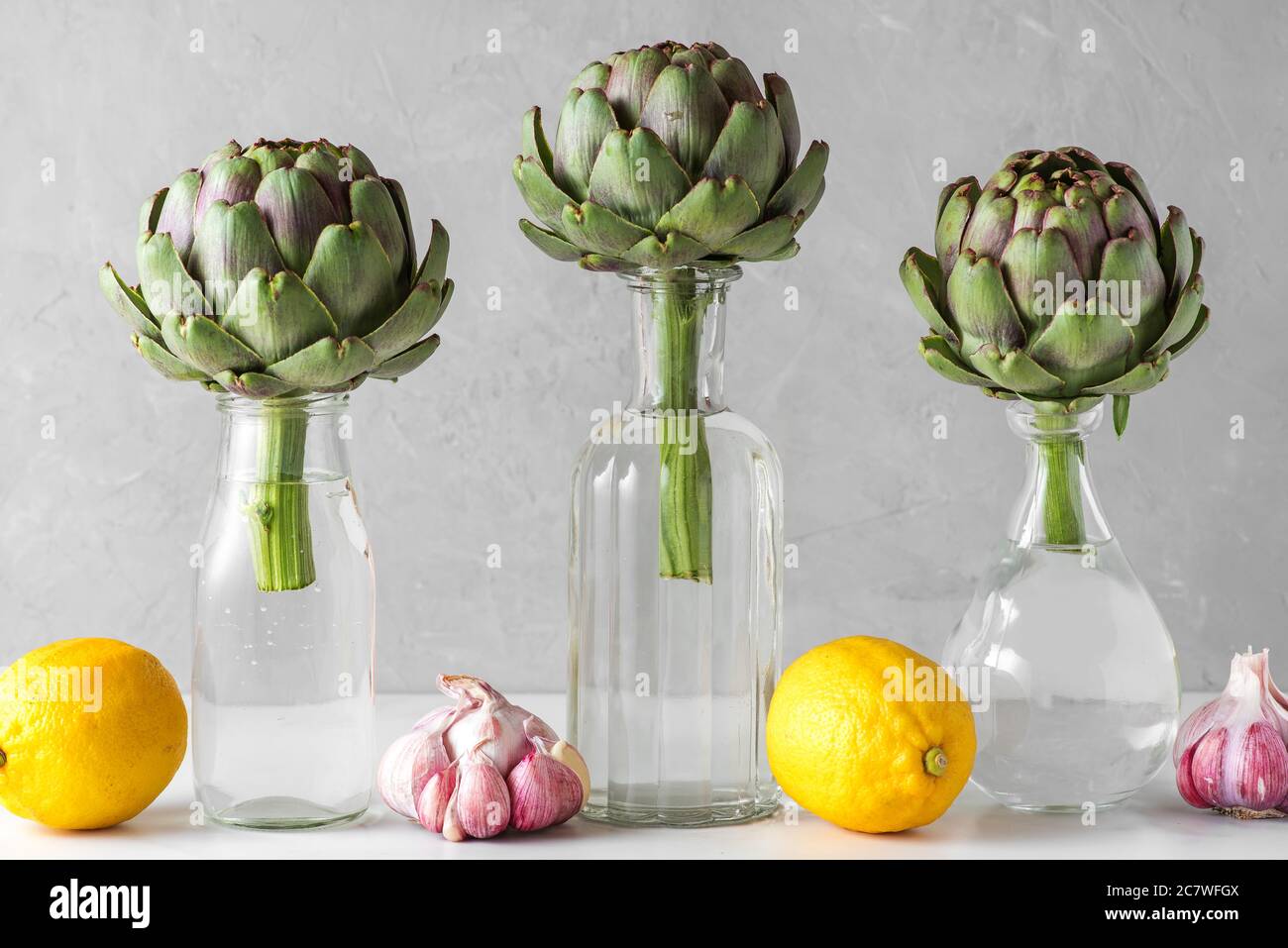 Artichoke vegetables in the bottles with lemons and garlic on white background. Creative modern food still life. Minimal concept Stock Photo