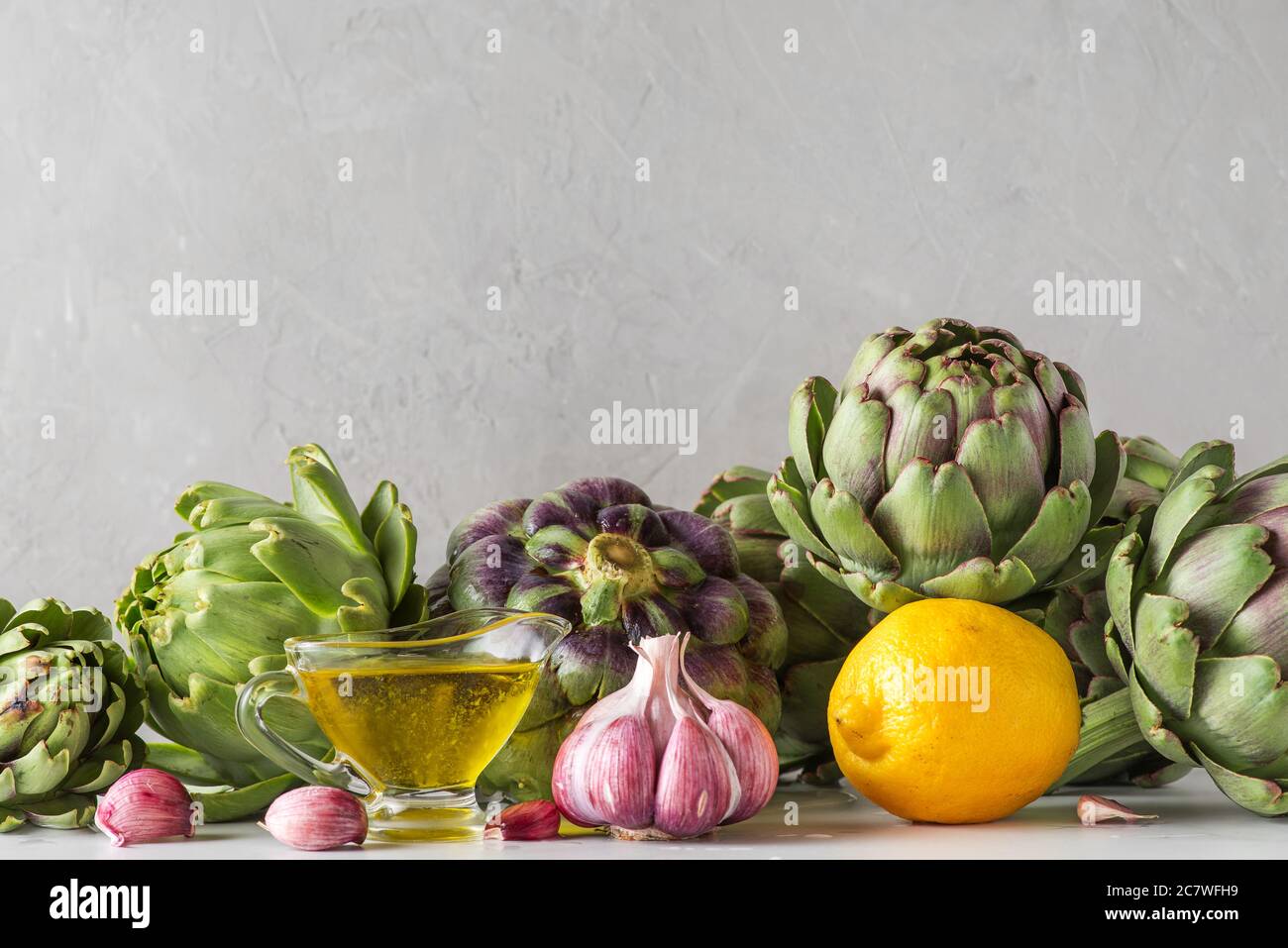 Healthy vegan food concept. Fresh ripe artichokes with olive oil, lemon and garlic on concrete background. Italian cuisine cooking background. close u Stock Photo