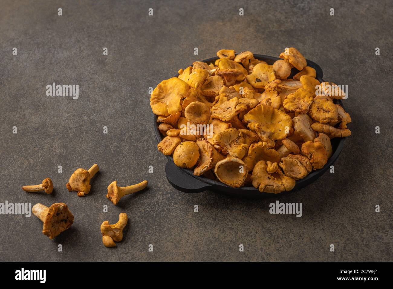 Raw fresh chanterelle fox mushrooms in a cast-iron frying pan on a wooden background. Copy space for text  Stock Photo