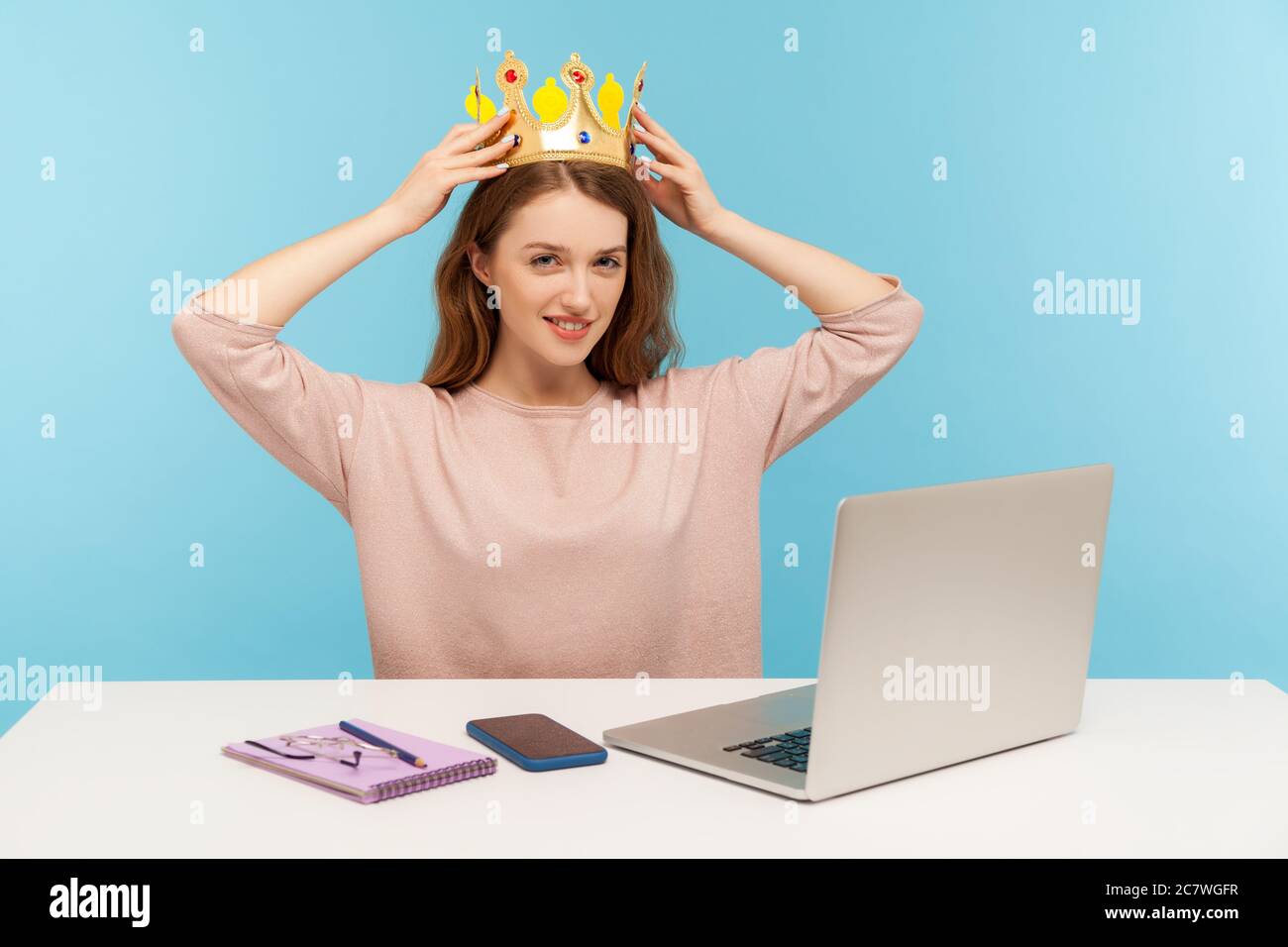 I am best. Self pride concept. Ambitious confident woman, successful employee putting crown on head, sitting in office workplace and smiling to camera Stock Photo