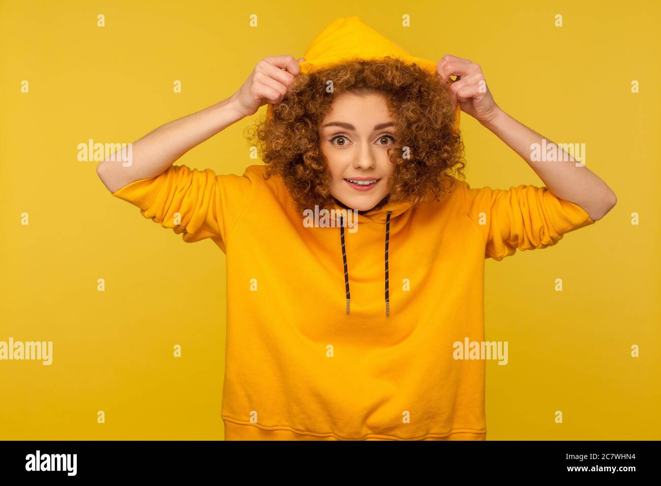 Portrait of funny positive girl with curly hair wearing urban style hoodie, putting on hood and smiling at camera, youth sport style female fashion. i Stock Photo