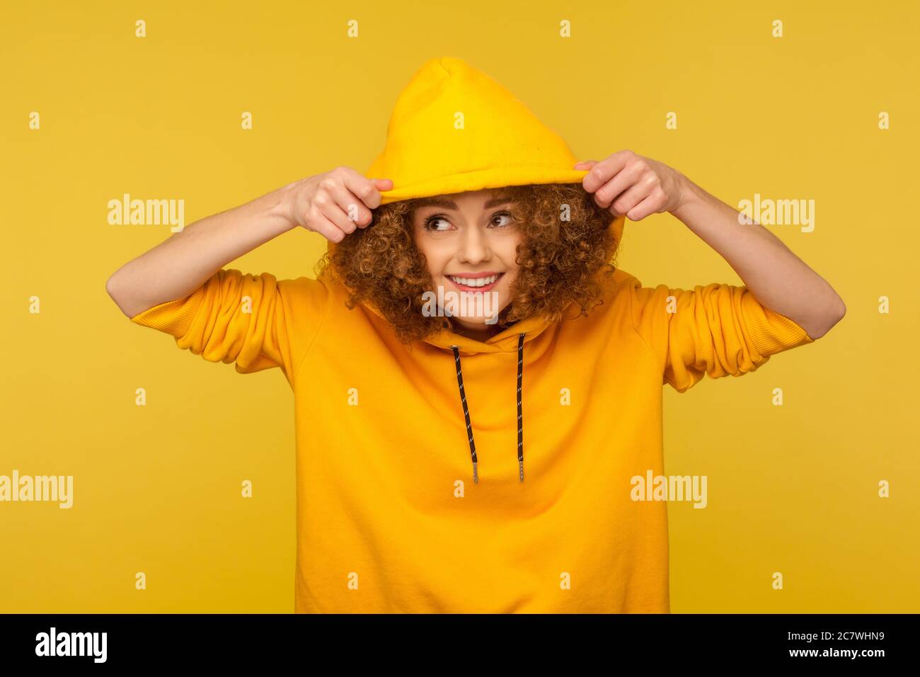 Portrait of funny smiling girl with curly hair wearing urban style hoodie, putting on hood and looking around, youth sport style female fashion. indoo Stock Photo