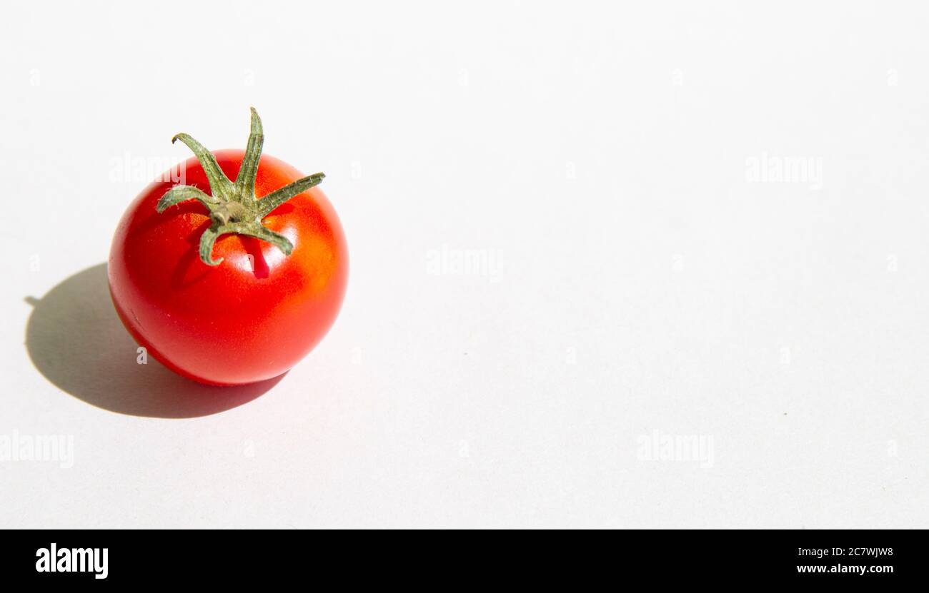 One red cherry tomato with green stems and tough shadow on a white background.copyspace for text Stock Photo