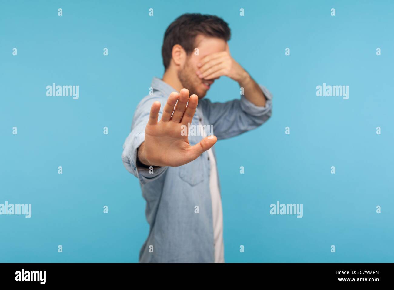 No, don't want to watch! Portrait of confused shy man in worker denim shirt covering eyes showing stop gesture, refusing to look at shameful content, Stock Photo