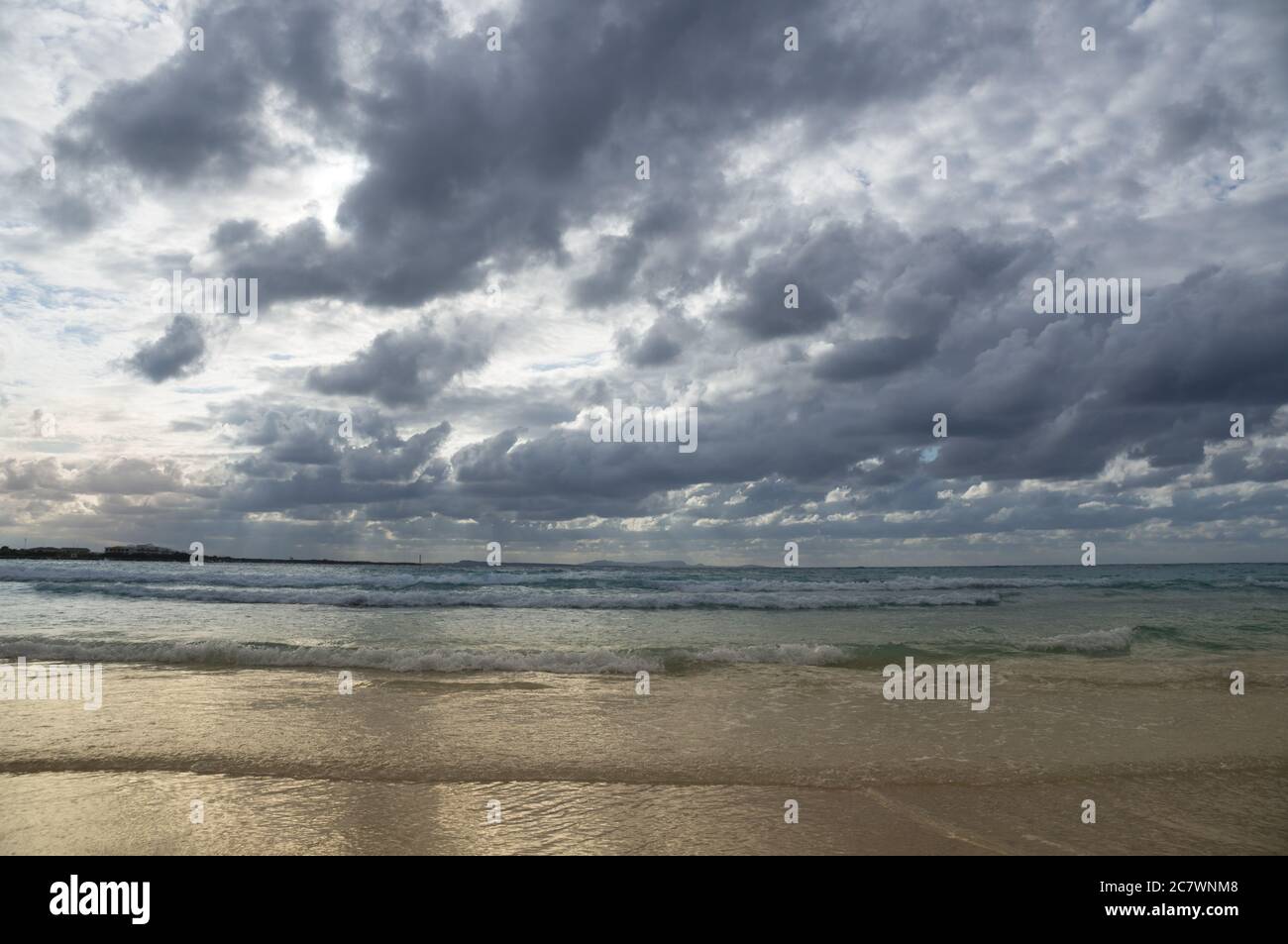 Stormy dark clouds above the sea with sandy beach and curling waves ...