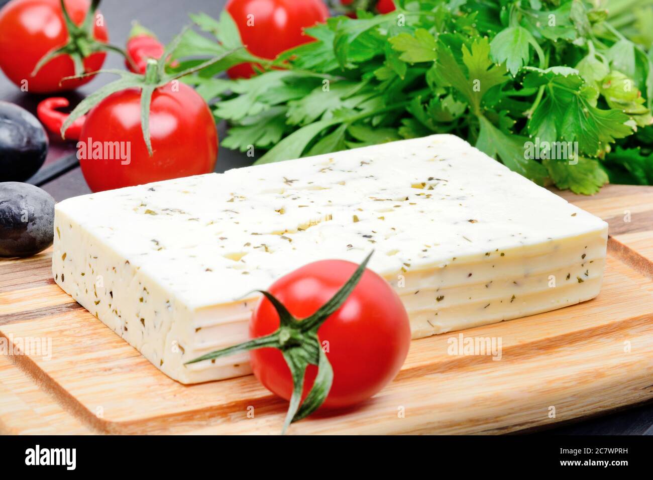 Close up of cheese with herbs and vegetables on cutting board Stock Photo