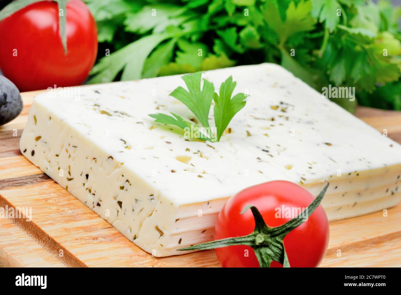 Close up of cheese with herbs and tomatoes on cutting board Stock Photo