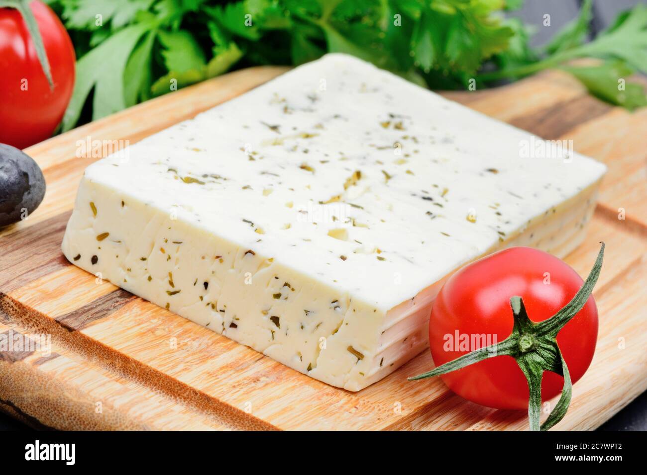 Cheese with herbs, olive and cherry tomatoes on cutting board Stock Photo