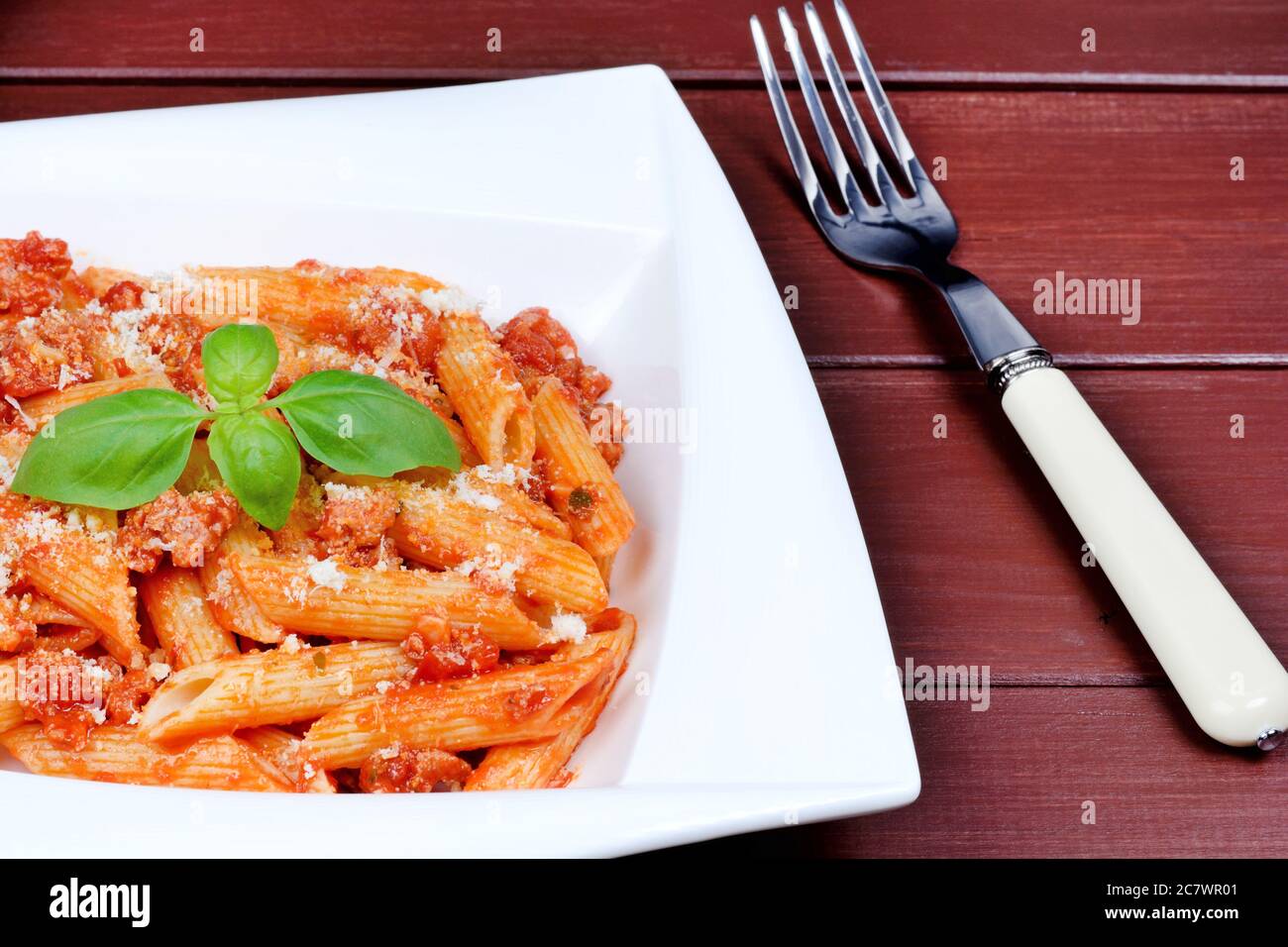 Penne with tomatoes sauce and parmesan in a plate on wooden table Stock Photo