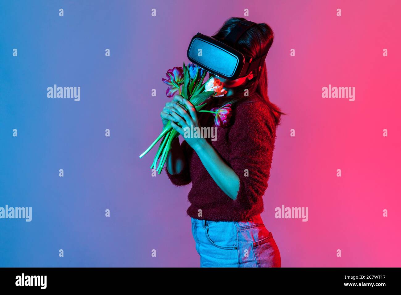 Lovely girl in VR glasses headset enjoying smell of flowers bouquet and