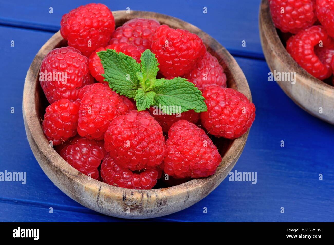 Fresh raspberries in a bowl on blue wood table Stock Photo