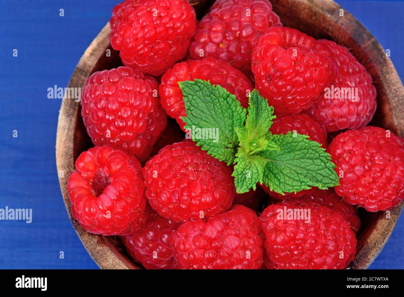 Delicious fresh raspberries in a bowl on blue wooden table Stock Photo