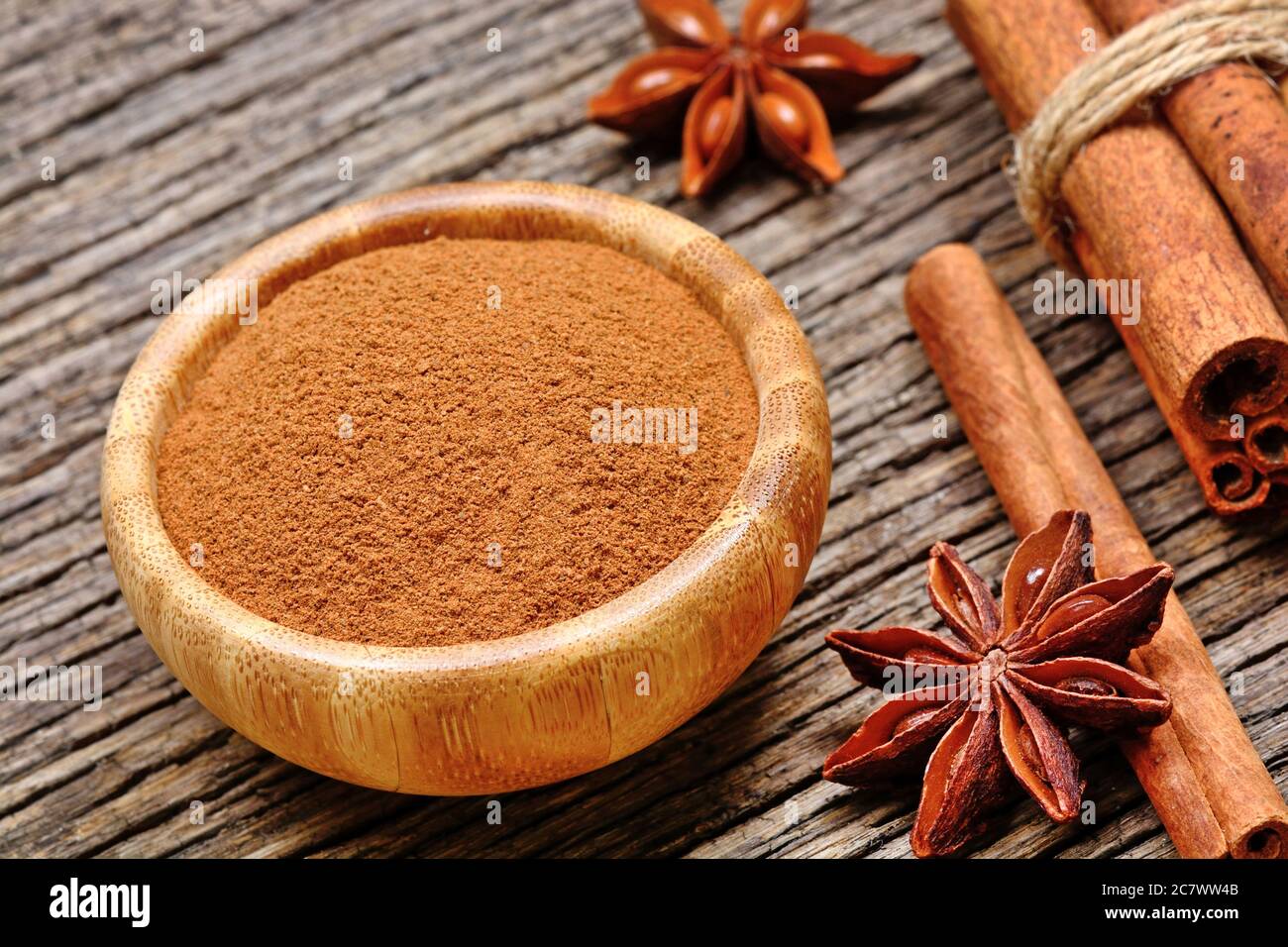 Cinnamon powder in a bamboo bowl with star anise and cinnamon sticks on a wood table Stock Photo