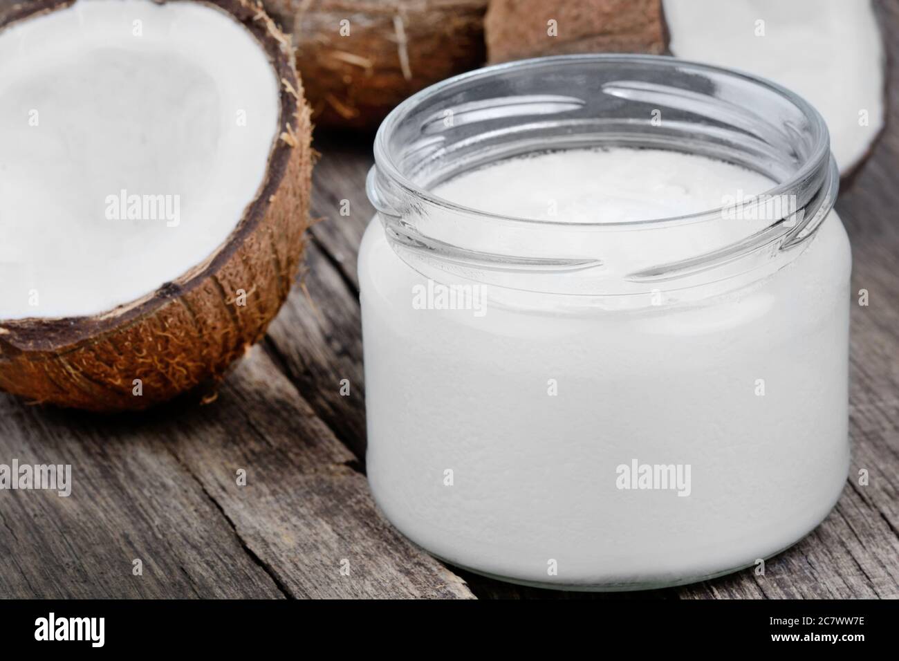 Coconut oil in a jar and fresh coconuts on wooden table Stock Photo