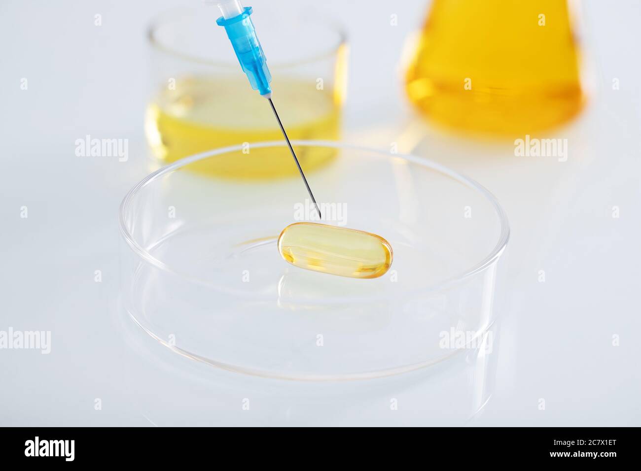 Closeup shot of a syringe injecting a clear yellow capsule in a glass ...