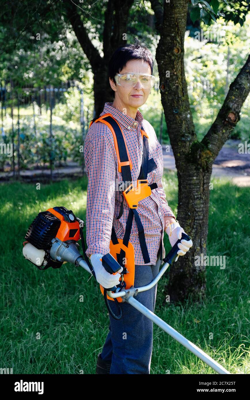 Portrait of female gardener with grass trimmer in the backyard. Garden work concept. Stock Photo