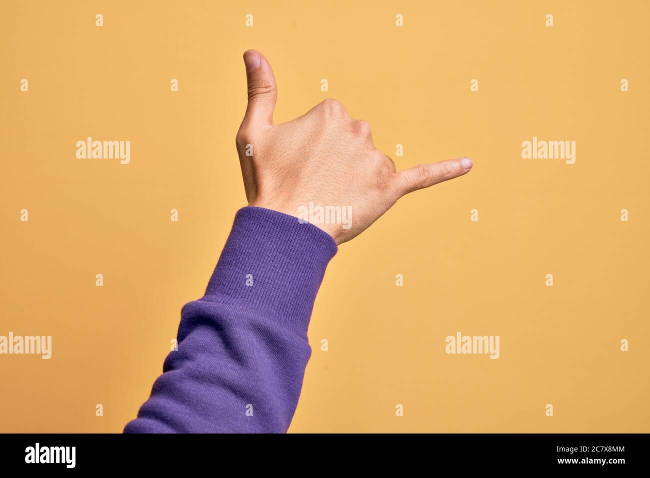 Hand of caucasian young man showing fingers over isolated yellow background gesturing Hawaiian shaka greeting gesture, telephone and communication sym Stock Photo